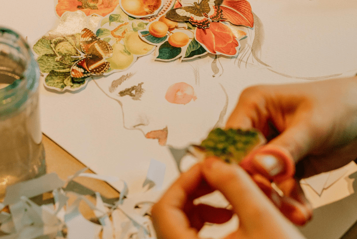 Hands creating a floral paper collage portrait.