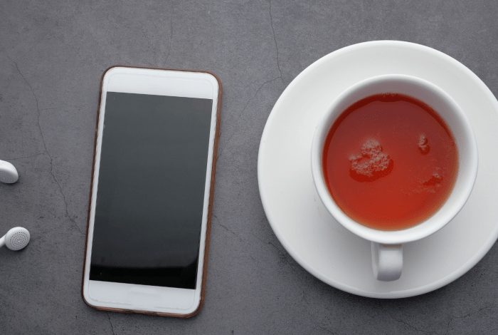 A smartphone, headphones and a cup of tea placed on a gray surface.