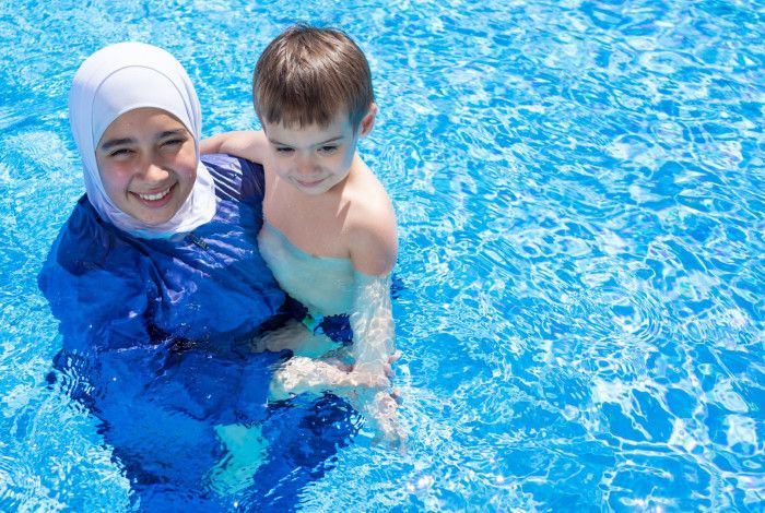 Parent wearing a hijab holding a child in the pool