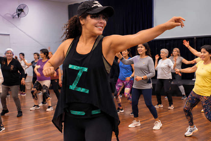A woman teaching Zumba class, surrounded by her students, mostly older ladies. 