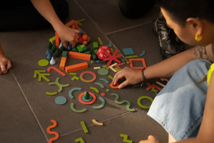 Two people playing with colourful wooden blocks on the ground. 