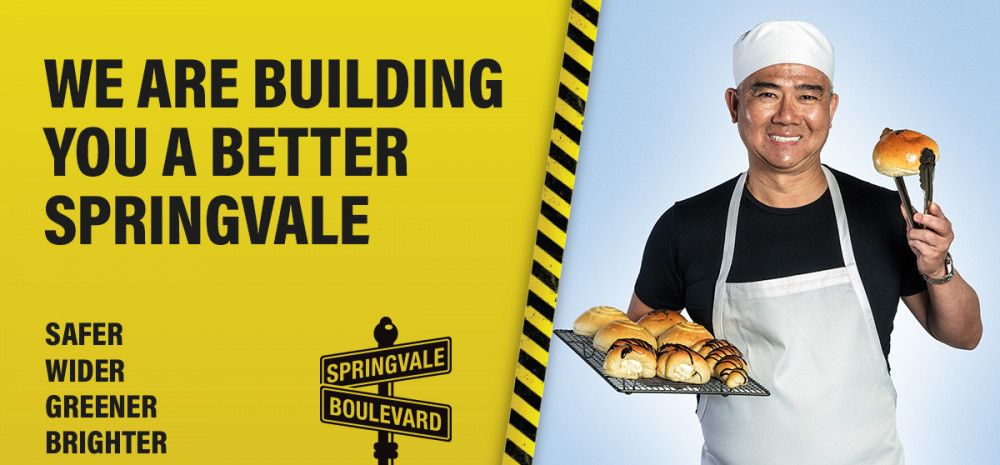 Baker holding bun with the text 'we are building you a better Springvale'