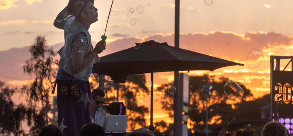 a stilt walker standing above a crowd blowing large bubbles