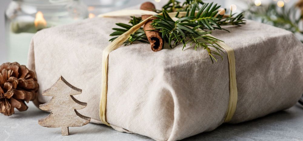 a gift wrapped in fabric and decorated with foliage and a pinecone