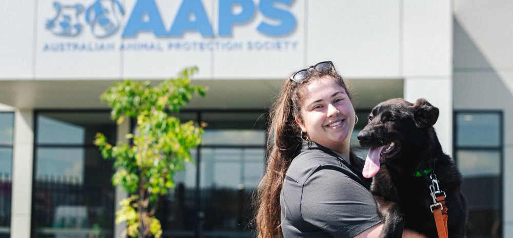 Happy woman hugging a dog in front of the AAPS building.