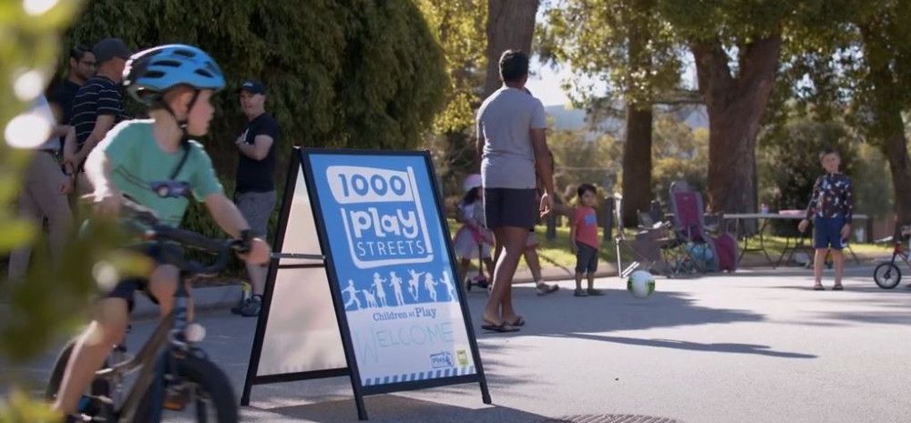 A child riding his bike past a 1000 Play Streets sign