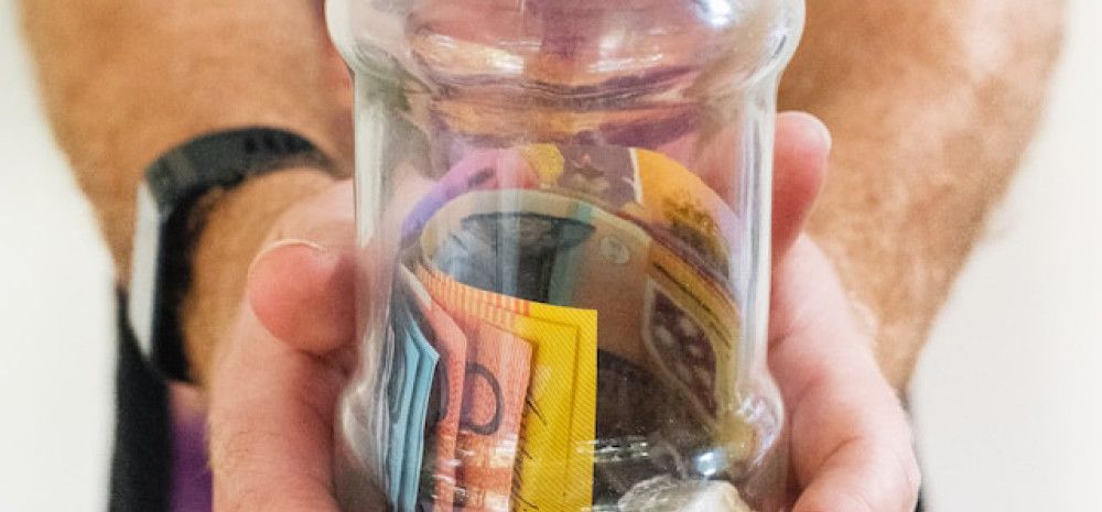 Man's hands holding glass jar full of money.