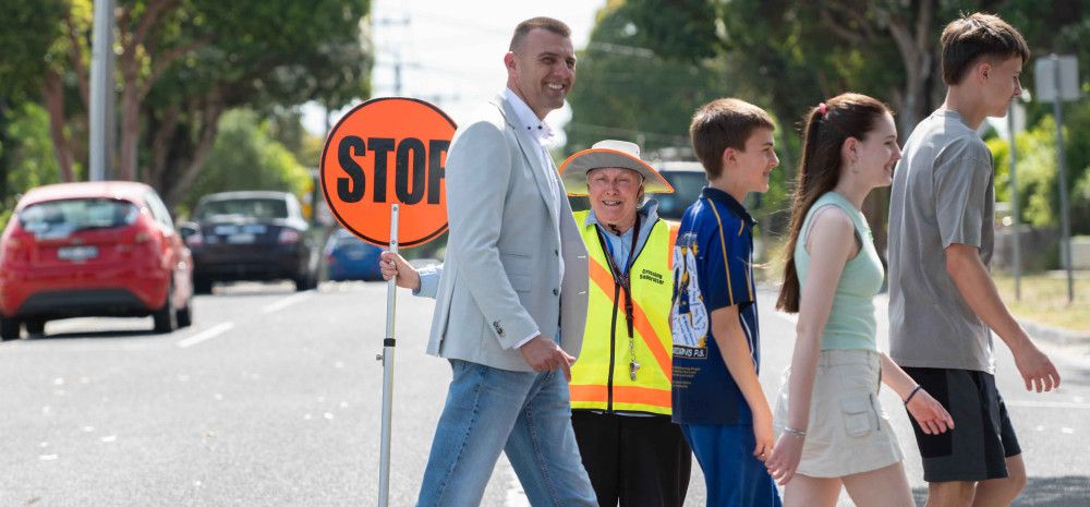 People crossing a pedestrian crossing in front of a supervisor with an orange stop sign.