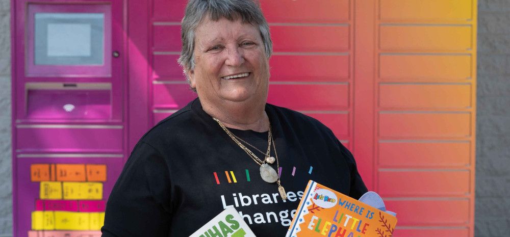 Councillor Angela Long holding children's books in front of the little library lockers