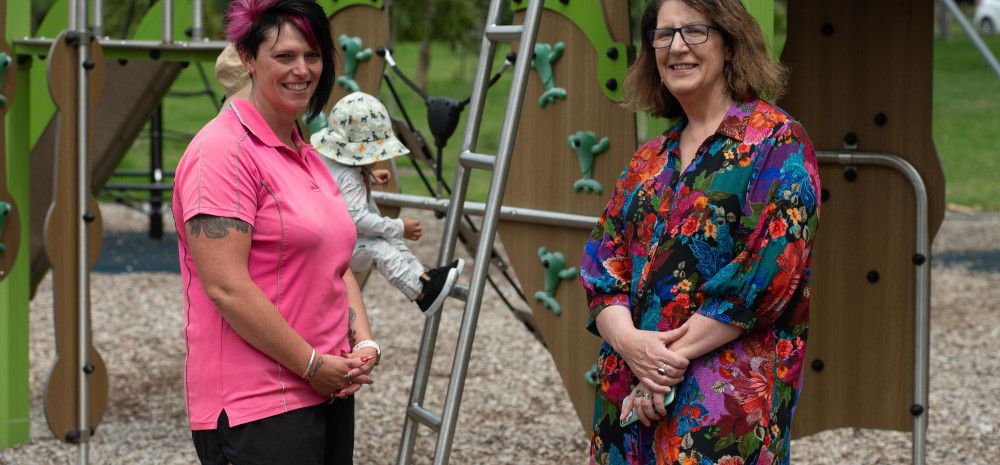 Councillor Rhonda Garad and another lady stand in front of a young child playing at a playground.