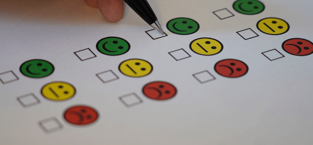Green, yellow and red smiley icons on paper. A person is ticking the green happy icon.