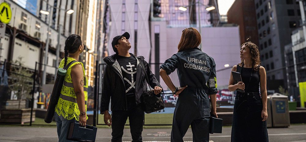 4 people standing in an urban environment. One wears a jumpsuit that says Urban code makers.