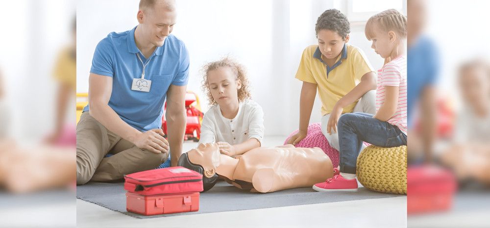 Trainer and group of children practising first aid on a mannequin.