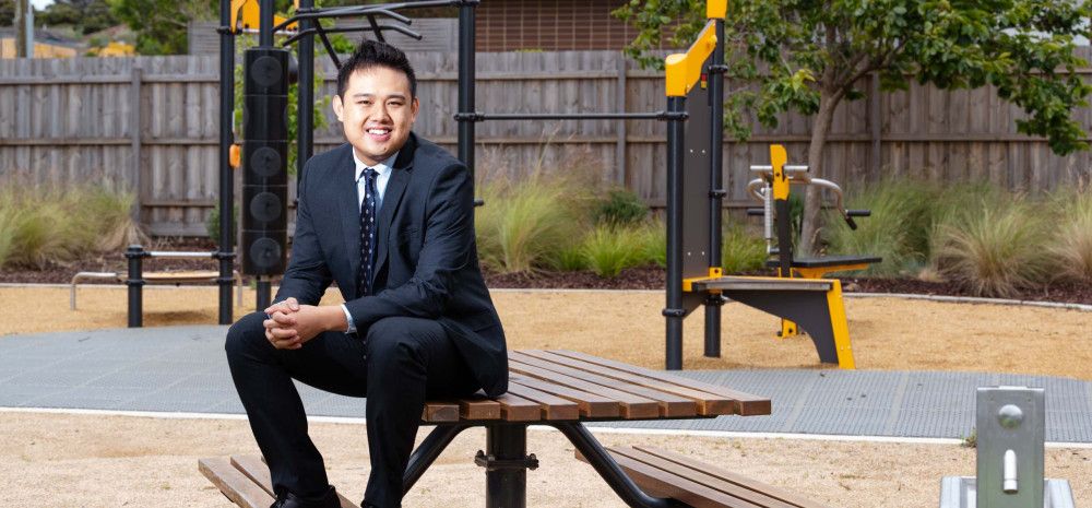 A man in a suit sits on a picnic table in front of play equipment