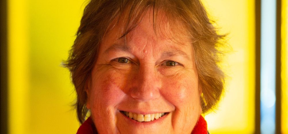 Close up of a smiling woman with short brown hair against a bright yellow backdrop.