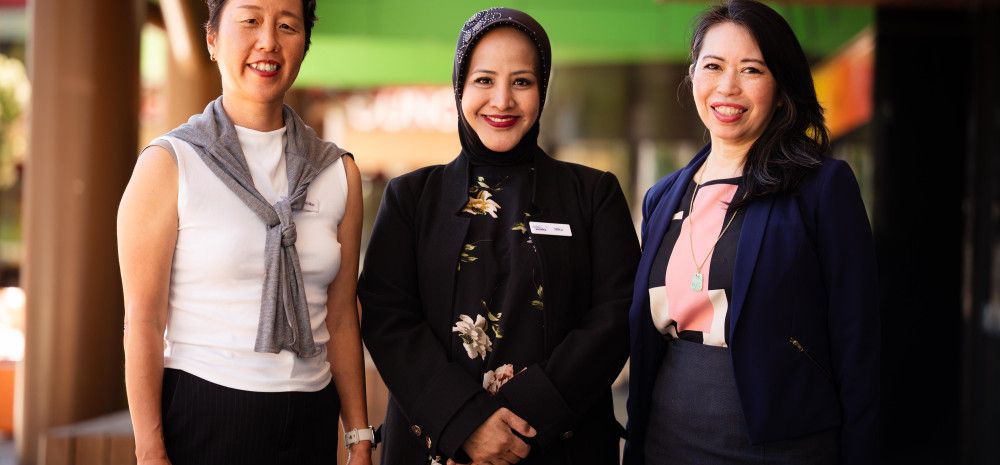 Three women stand in a line and smile at the camera