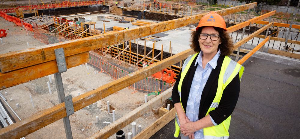 A woman dressed in a high vis vest and a hard hat stands on a platform overlooking a worksite