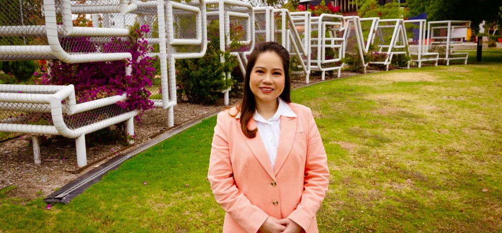A woman dressed in a light pink blazer standing in front of a metal sculpture spelling out Springvale