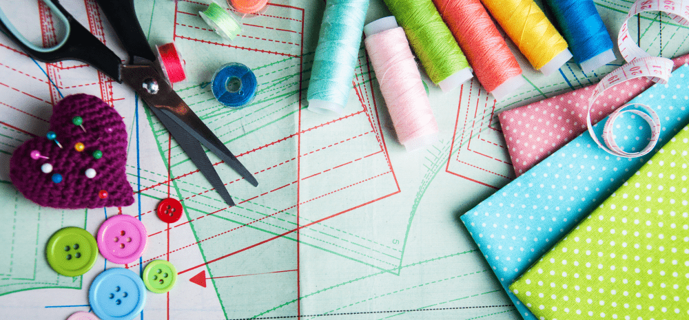 A collection of buttons, threads, fabrics and scissors laid out on sewing patterns. 