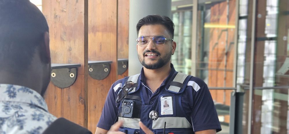 A man dressed in a security uniform talks to another man whose back is to the camera