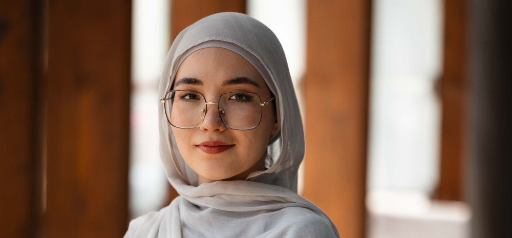 A woman wearing a head scarf and glasses smiles at the camera