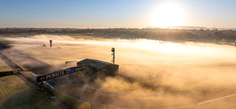 Looking down over the home straight of a racing track that is covered in mist as the sun rises.