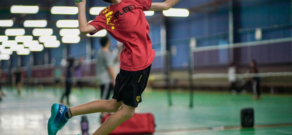 A boy wearing red top playing badminton.
