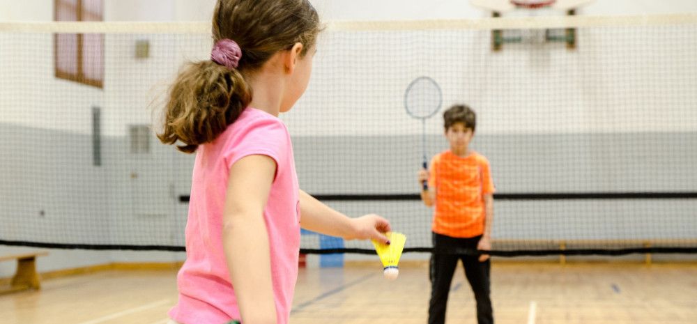 A gidl wearing pink top playing badminton with a boy wearing orange top.