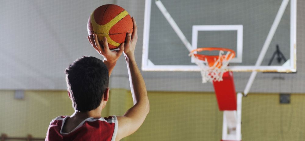A boy wearing red top is trying to shoot a basketball to the basketball hoop.