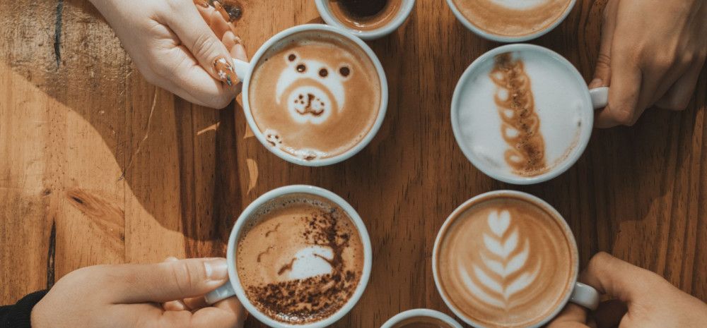 hands holding four coffees on table