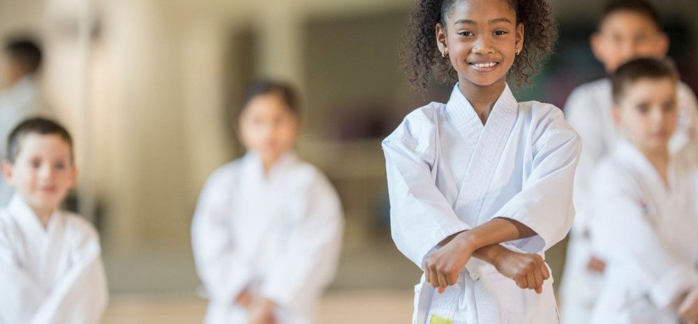 A girl smiling, doing a karate post and wearing white karate uniform, with four boys standing at the background.