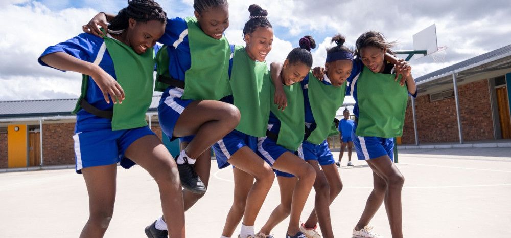 Six girls wearing netball uniform jumping around happily