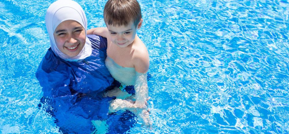 Parent wearing a hijab holding a child in the pool