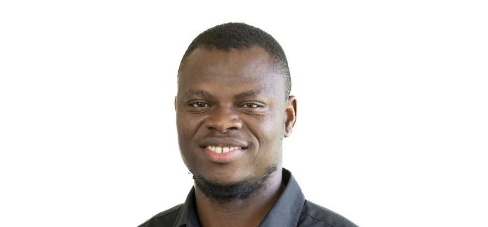 A smiling man dressed in a black shirt against a plain white background.
