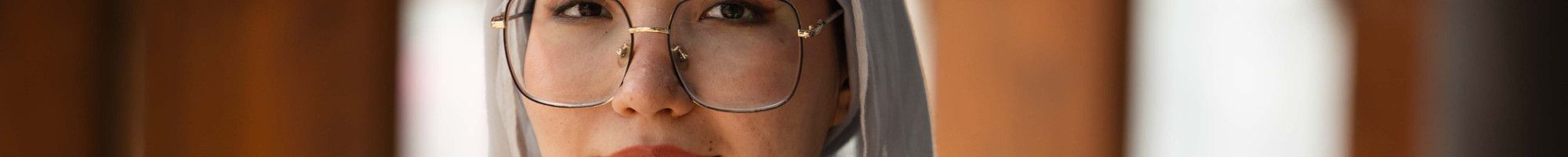A woman wearing a head scarf and glasses smiles at the camera