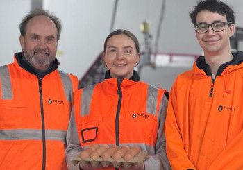Three people smiling and holding a carton of eggs