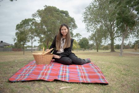 Smiling woman sitting on a picnic rug while opening a wicker picnic basket