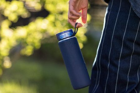A blue reusable water bottle hanging from the hand of someone walking in a park