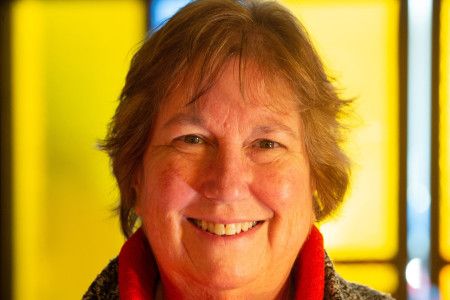 Close up of a smiling woman with short brown hair against a bright yellow backdrop.