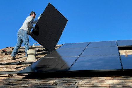 A man installing solar panels on the roof of a house