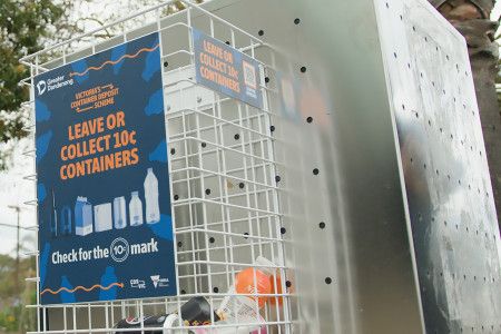 A small cage attached to the side of a stainless steel rubbish bin with a sign that reads “Leave or collect 10 cent containers”.