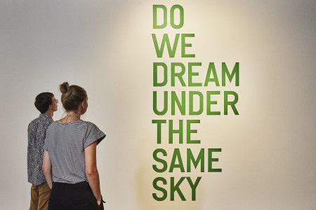 People standing in front of a sign 'Do we dream under the same sky'