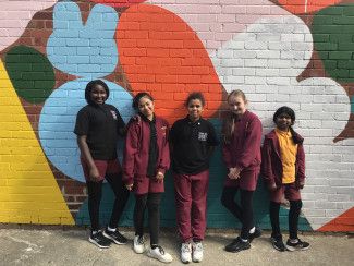 Children standing in front of the brick wall with coloured shapes completed