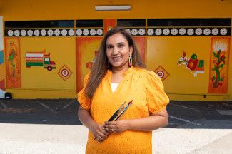 Yoge Biju standing in front of her mural 'The Village'