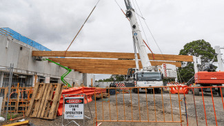 A crane lowers a massive timber bean into place at Oasis Aquatics and Wellbeing