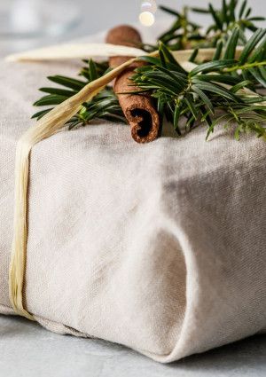 a gift wrapped in fabric and decorated with foliage and a pinecone